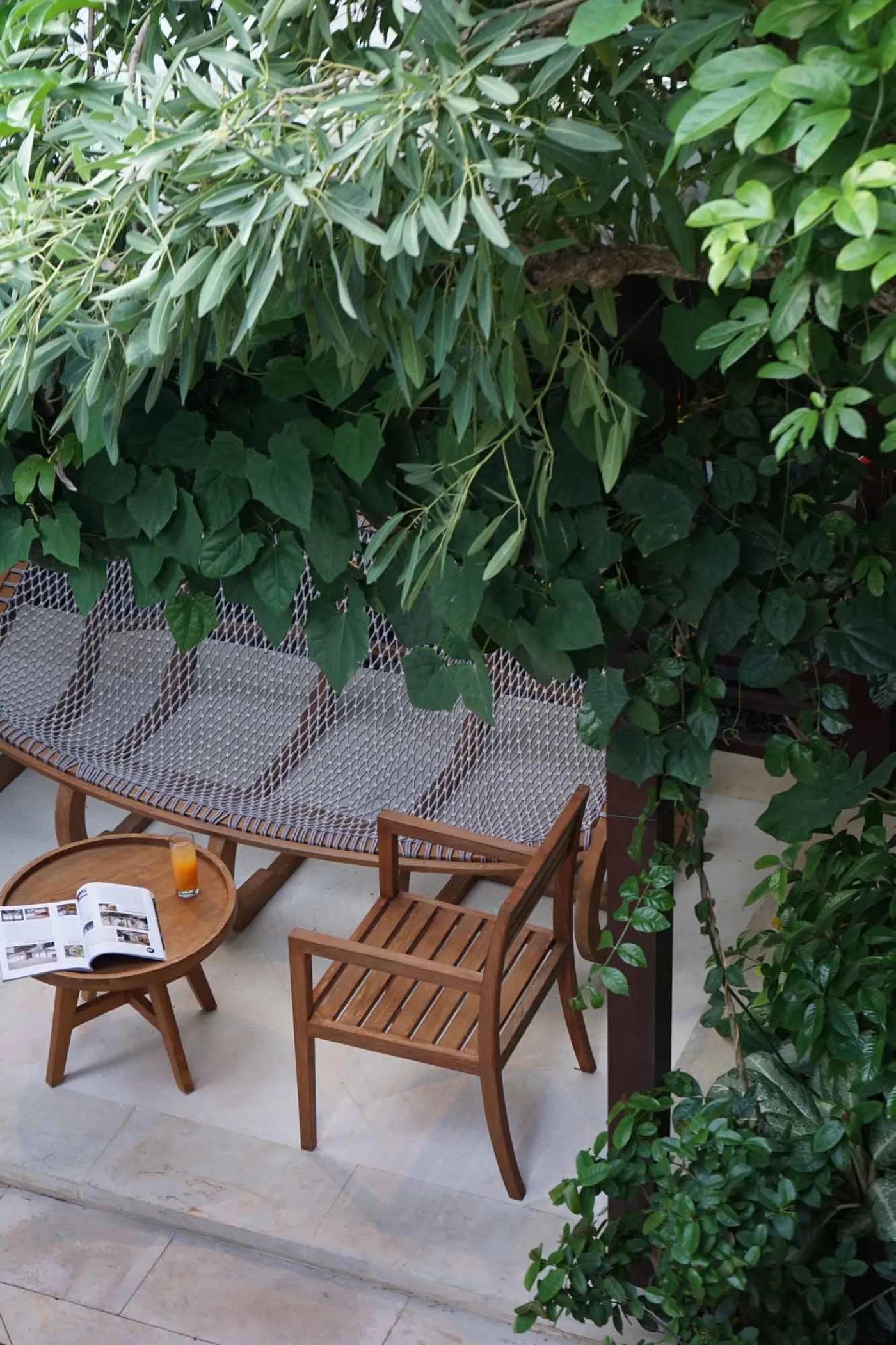 Balinese villa interior featuring a woven thatched hanging lamp, open white kitchen, and vibrant rooster wall art over a wooden dining table. - Bali Villas
