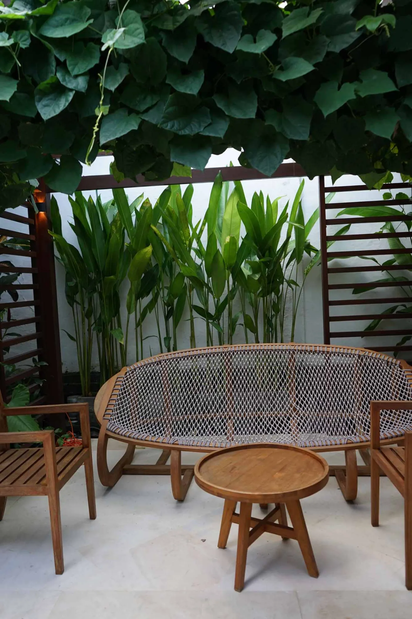 Balinese villa interior featuring a woven thatched hanging lamp, open white kitchen, and vibrant rooster wall art over a wooden dining table. - Bali Villas