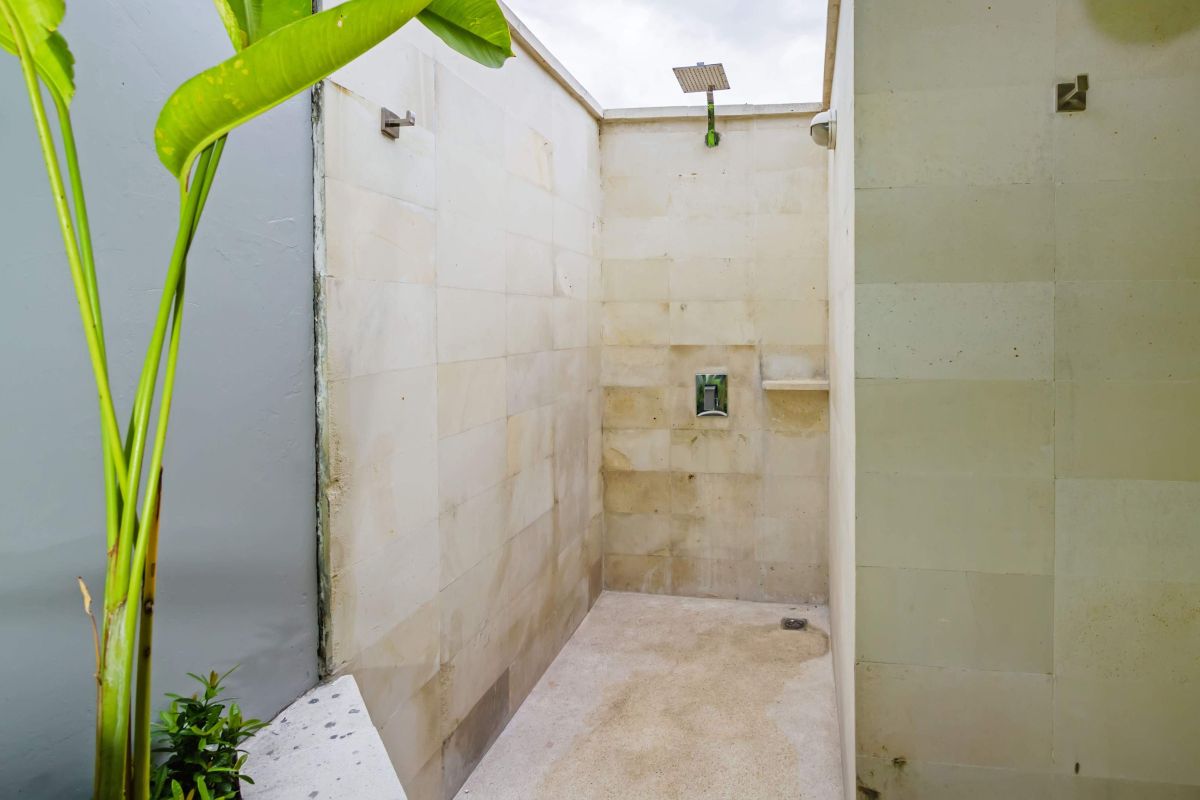 Modern Balinese-style kitchen with bamboo pendant lights, concrete island bar, white cabinets, tropical flower vase, and wooden statues. - Bali Villas