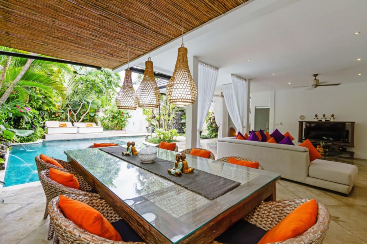 Modern Balinese-style kitchen with bamboo pendant lights, concrete island bar, white cabinets, tropical flower vase, and wooden statues. - Bali Villas