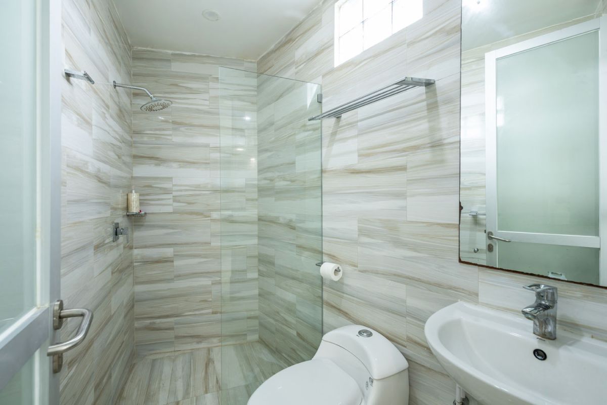 Spacious tropical villa veranda with curved thatched roof, wooden dining table and chairs, lush greenery, hanging drapes, and a serene lily pond. - Bali Villas