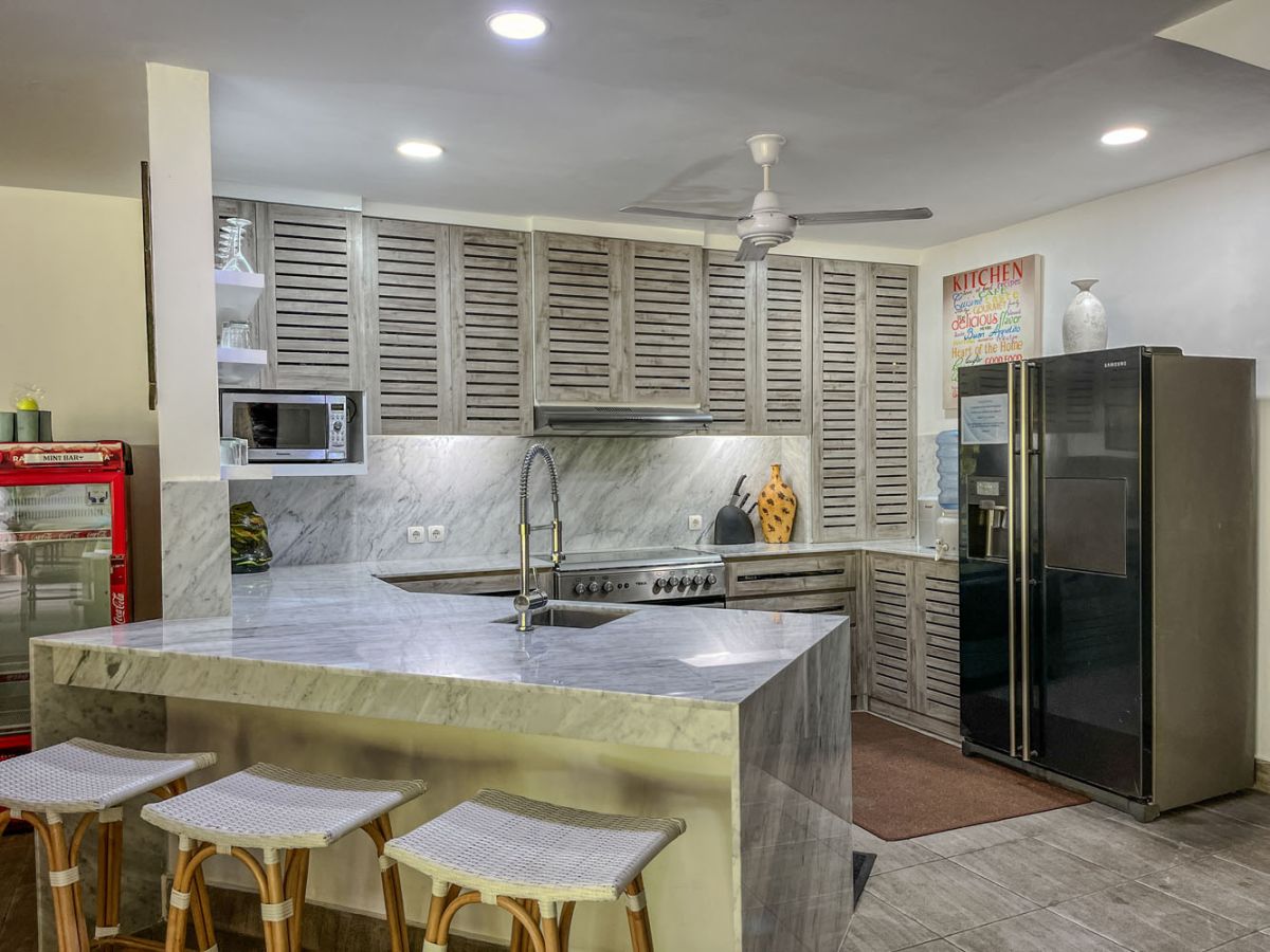 Spacious tropical villa veranda with curved thatched roof, wooden dining table and chairs, lush greenery, hanging drapes, and a serene lily pond. - Bali Villas