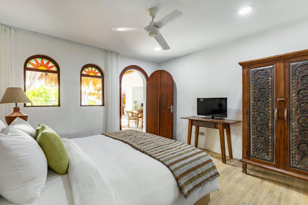 Spacious tropical villa veranda with curved thatched roof, wooden dining table and chairs, lush greenery, hanging drapes, and a serene lily pond. - Bali Villas