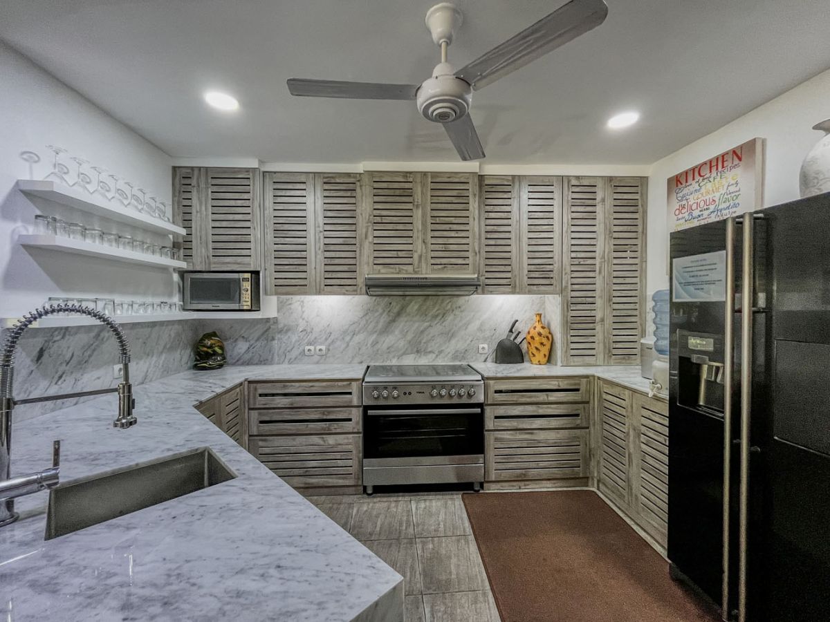 Spacious tropical villa veranda with curved thatched roof, wooden dining table and chairs, lush greenery, hanging drapes, and a serene lily pond. - Bali Villas