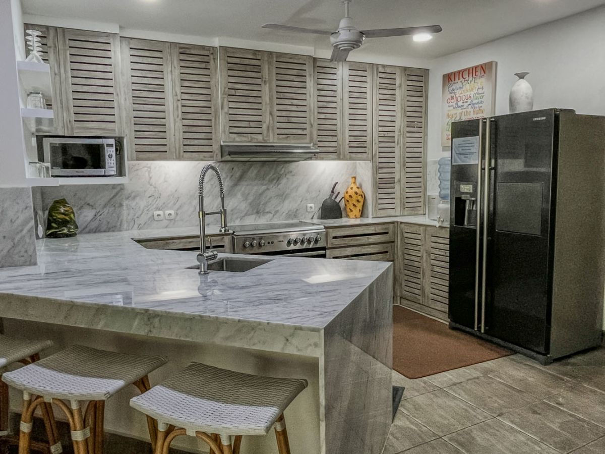 Spacious tropical villa veranda with curved thatched roof, wooden dining table and chairs, lush greenery, hanging drapes, and a serene lily pond. - Bali Villas