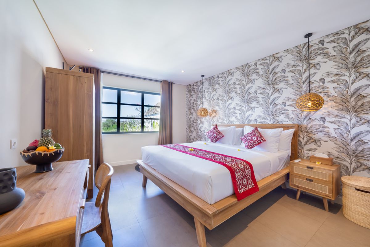 Elegant open-plan tropical kitchen with wooden cabinets, bamboo pendant lights, set dining table, and sliding glass doors to outdoor patio. - Bali Villas