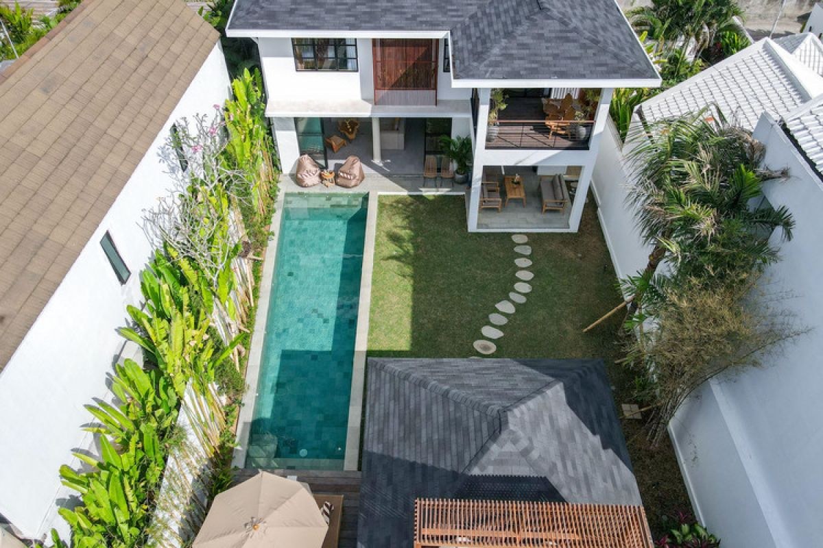 Elegant open-plan tropical kitchen with wooden cabinets, bamboo pendant lights, set dining table, and sliding glass doors to outdoor patio. - Bali Villas