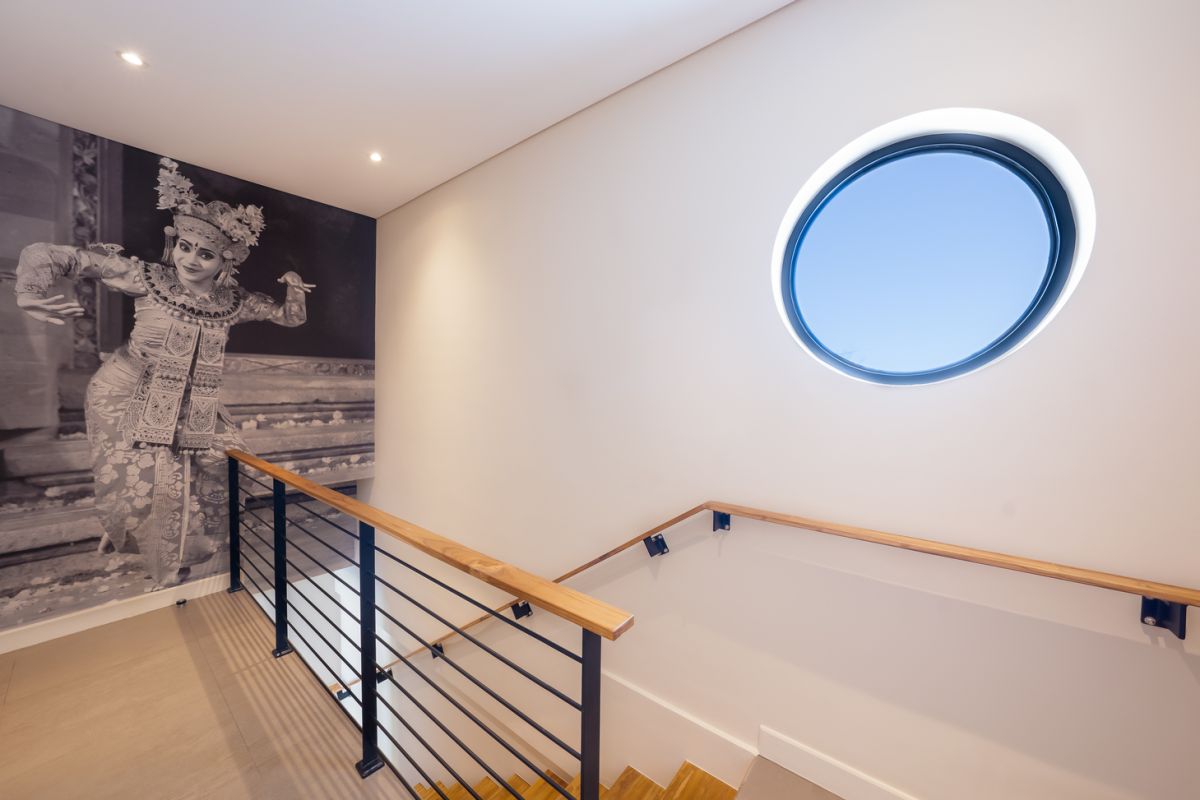 Elegant open-plan tropical kitchen with wooden cabinets, bamboo pendant lights, set dining table, and sliding glass doors to outdoor patio. - Bali Villas