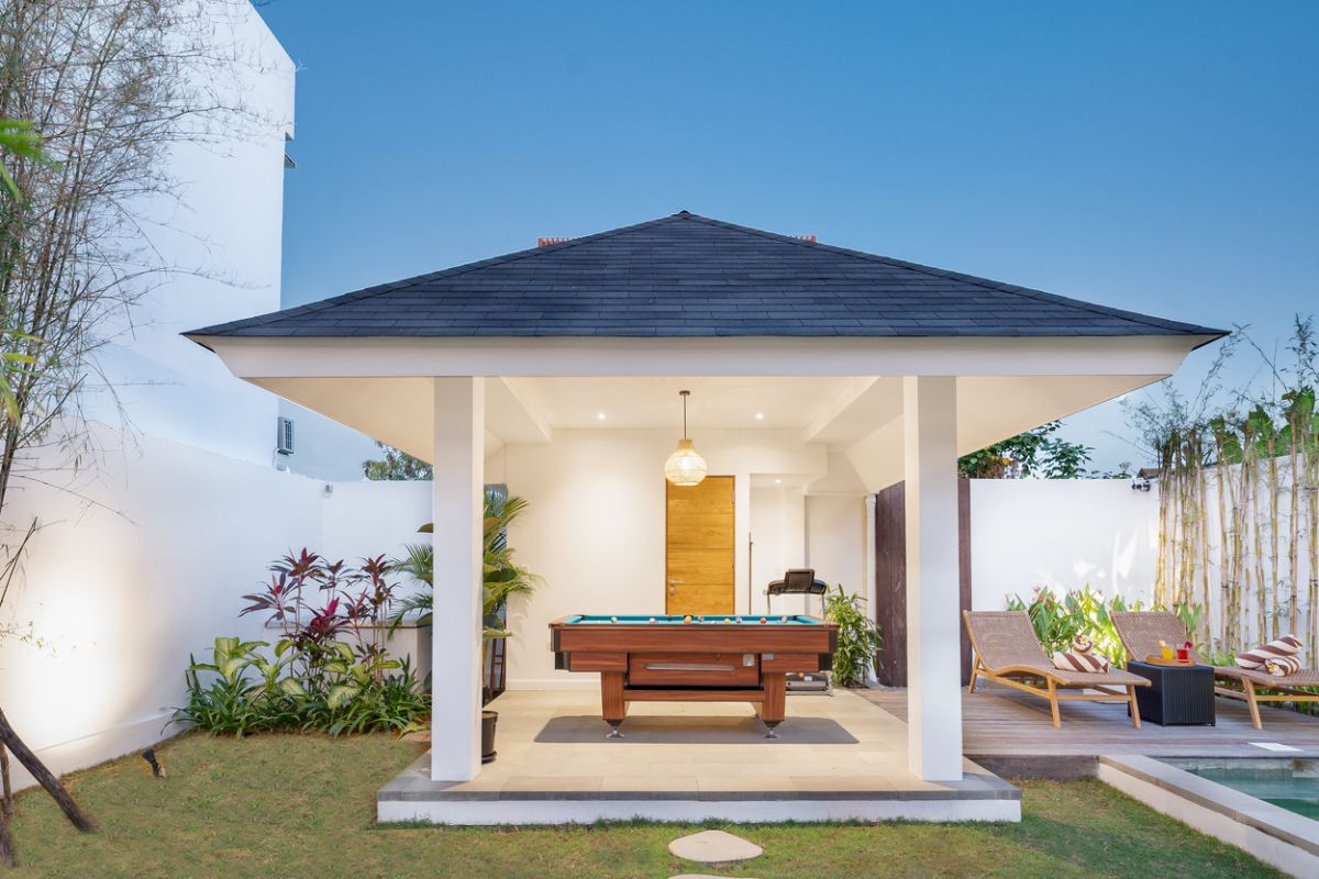 Elegant open-plan tropical kitchen with wooden cabinets, bamboo pendant lights, set dining table, and sliding glass doors to outdoor patio. - Bali Villas