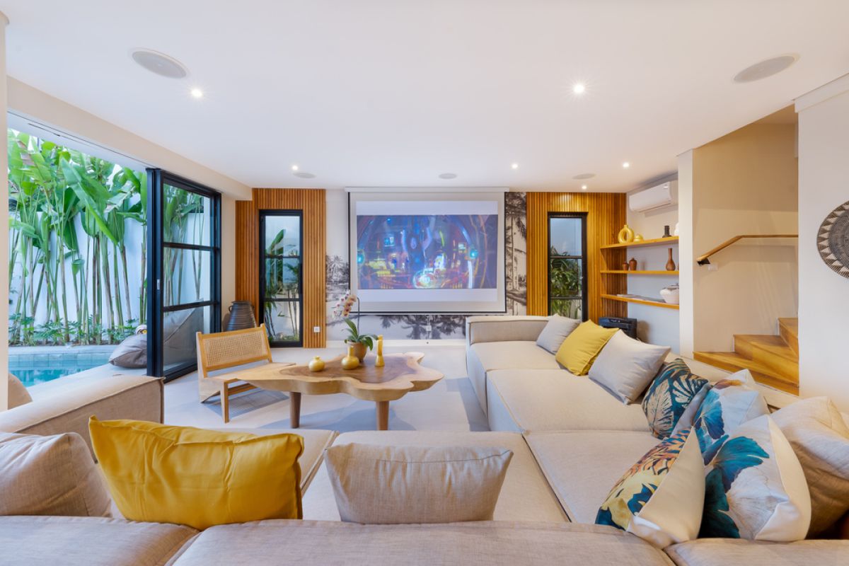 Elegant open-plan tropical kitchen with wooden cabinets, bamboo pendant lights, set dining table, and sliding glass doors to outdoor patio. - Bali Villas