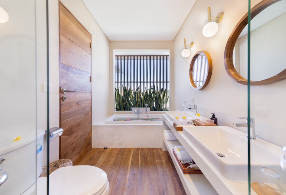 Elegant open-plan tropical kitchen with wooden cabinets, bamboo pendant lights, set dining table, and sliding glass doors to outdoor patio. - Bali Villas