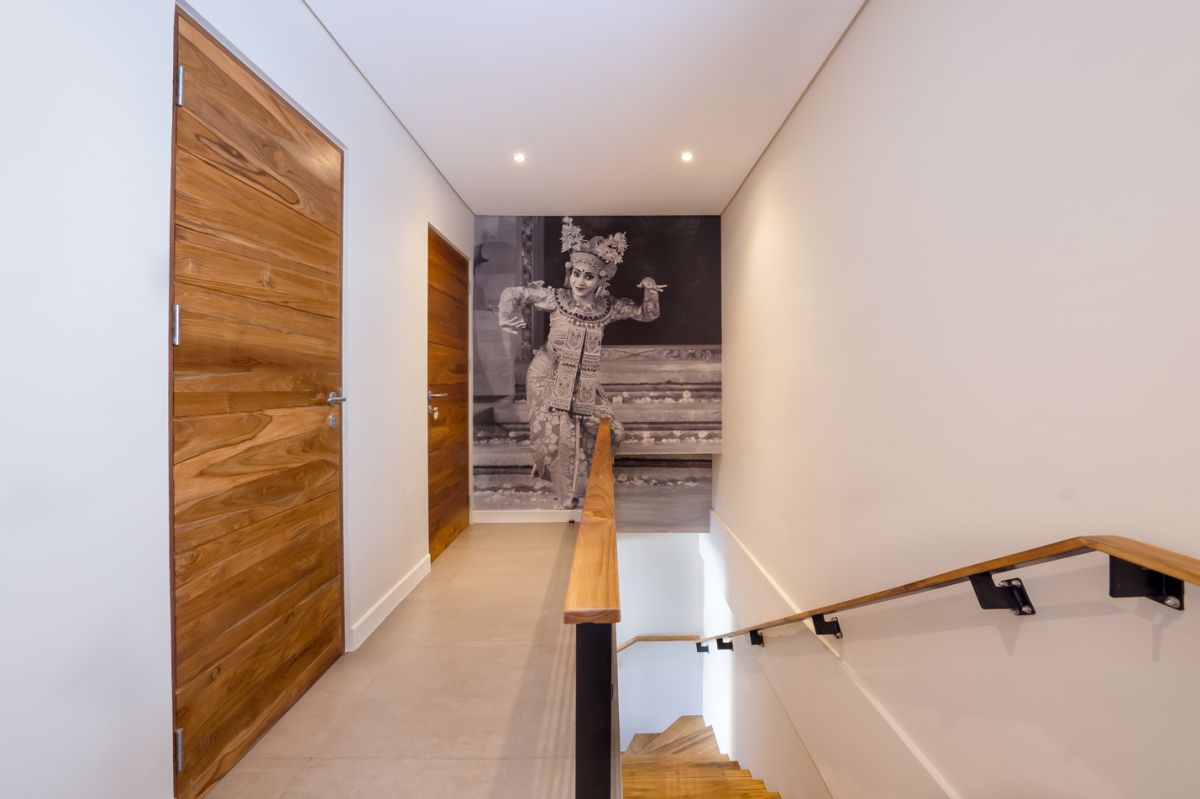 Elegant open-plan tropical kitchen with wooden cabinets, bamboo pendant lights, set dining table, and sliding glass doors to outdoor patio. - Bali Villas