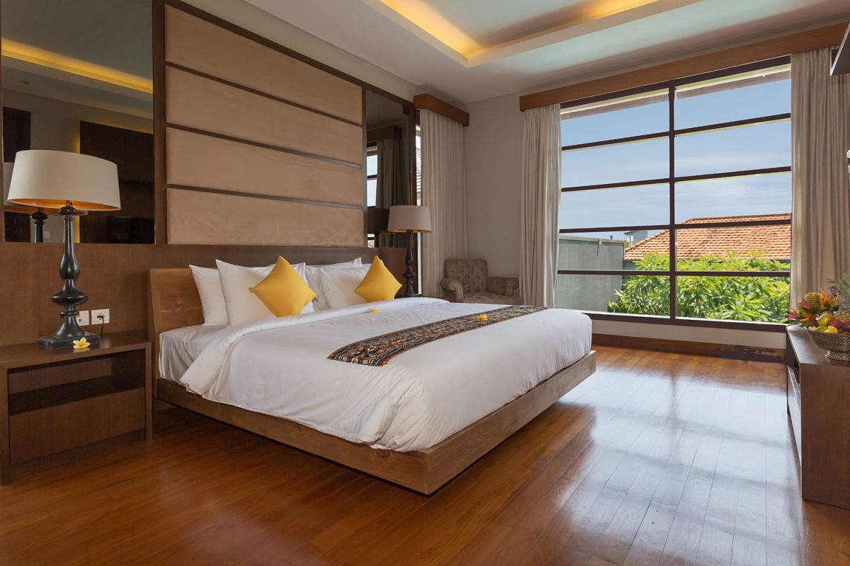 Luxurious spa bathroom with freestanding oval bathtub filled with pink water and rose petals, tropical bird-of-paradise flowers, white robe, and pebble wall accents. - Bali Villas
