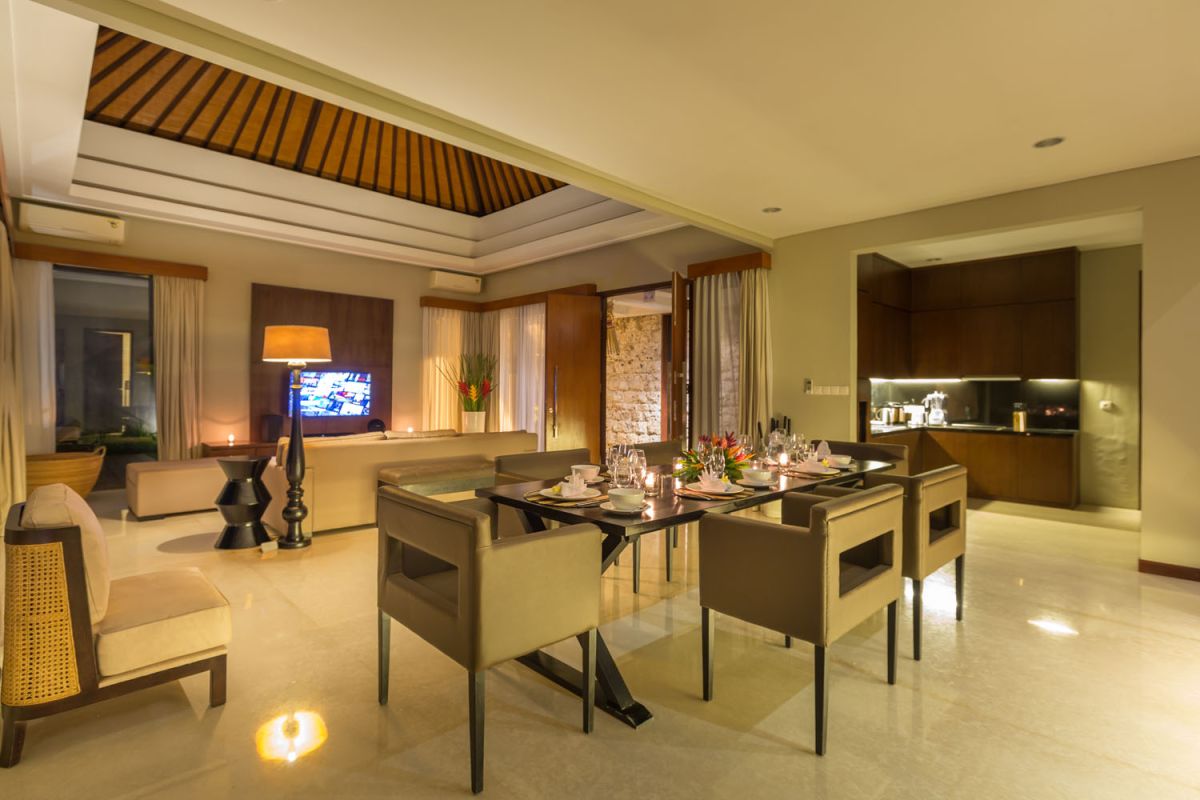 Luxurious spa bathroom with freestanding oval bathtub filled with pink water and rose petals, tropical bird-of-paradise flowers, white robe, and pebble wall accents. - Bali Villas