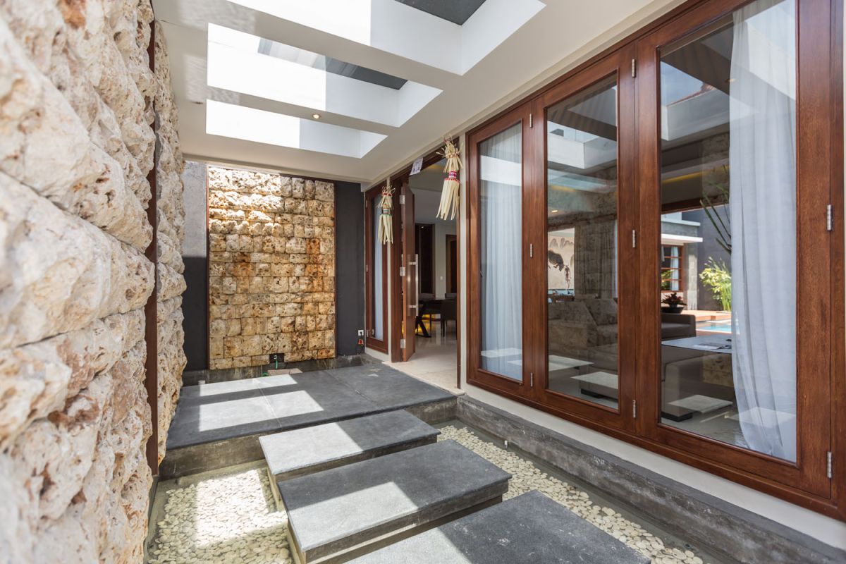 Luxurious spa bathroom with freestanding oval bathtub filled with pink water and rose petals, tropical bird-of-paradise flowers, white robe, and pebble wall accents. - Bali Villas