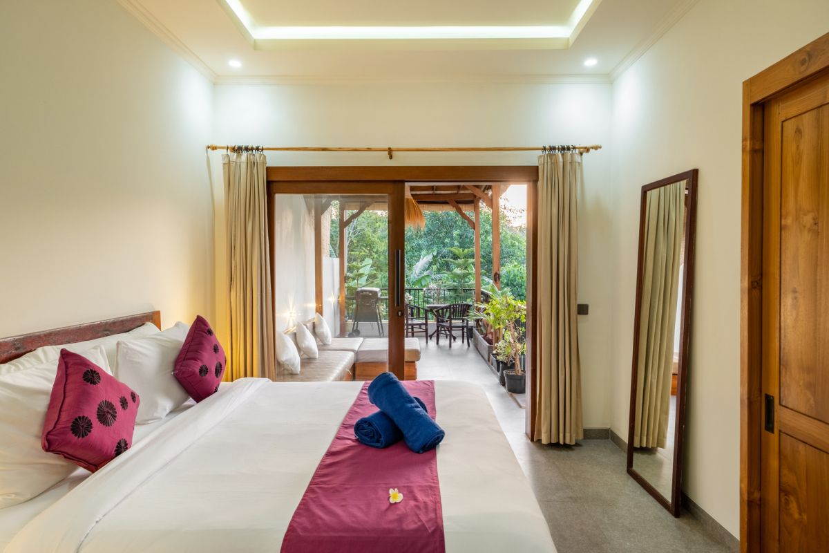 Overhead view of a private plunge pool in a tropical Bali villa, surrounded by wooden deck, lounge chairs, lush plants, and open bedroom doors. - Bali Villas