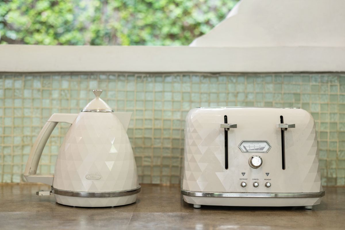 Modern white kitchen bar with concrete countertop, wooden stools, and lush tropical greenery outside arched windows. - Bali Villas