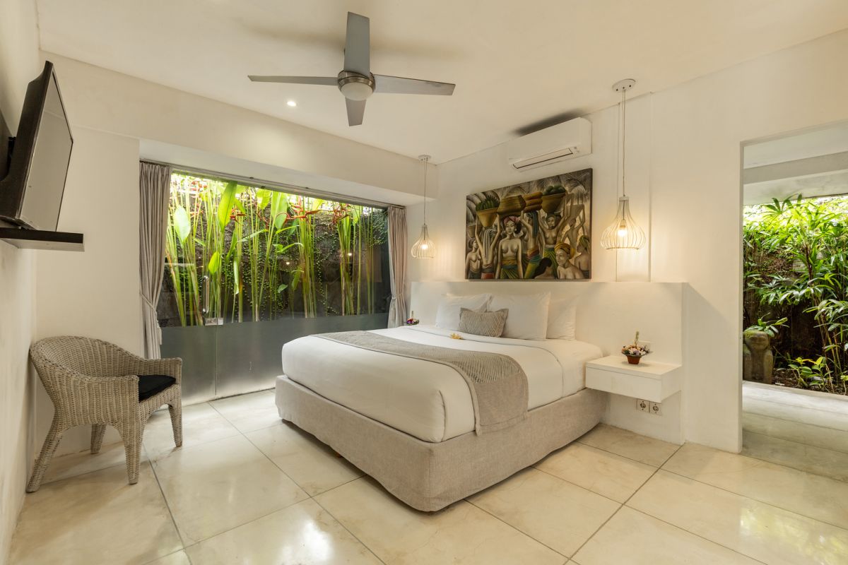 Modern white kitchen bar with concrete countertop, wooden stools, and lush tropical greenery outside arched windows. - Bali Villas