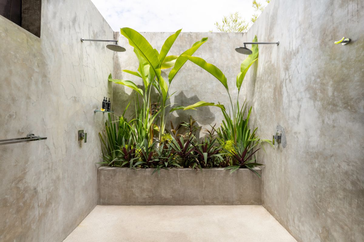 Modern white kitchen bar with concrete countertop, wooden stools, and lush tropical greenery outside arched windows. - Bali Villas