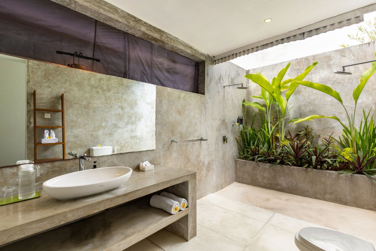 Modern white kitchen bar with concrete countertop, wooden stools, and lush tropical greenery outside arched windows. - Bali Villas