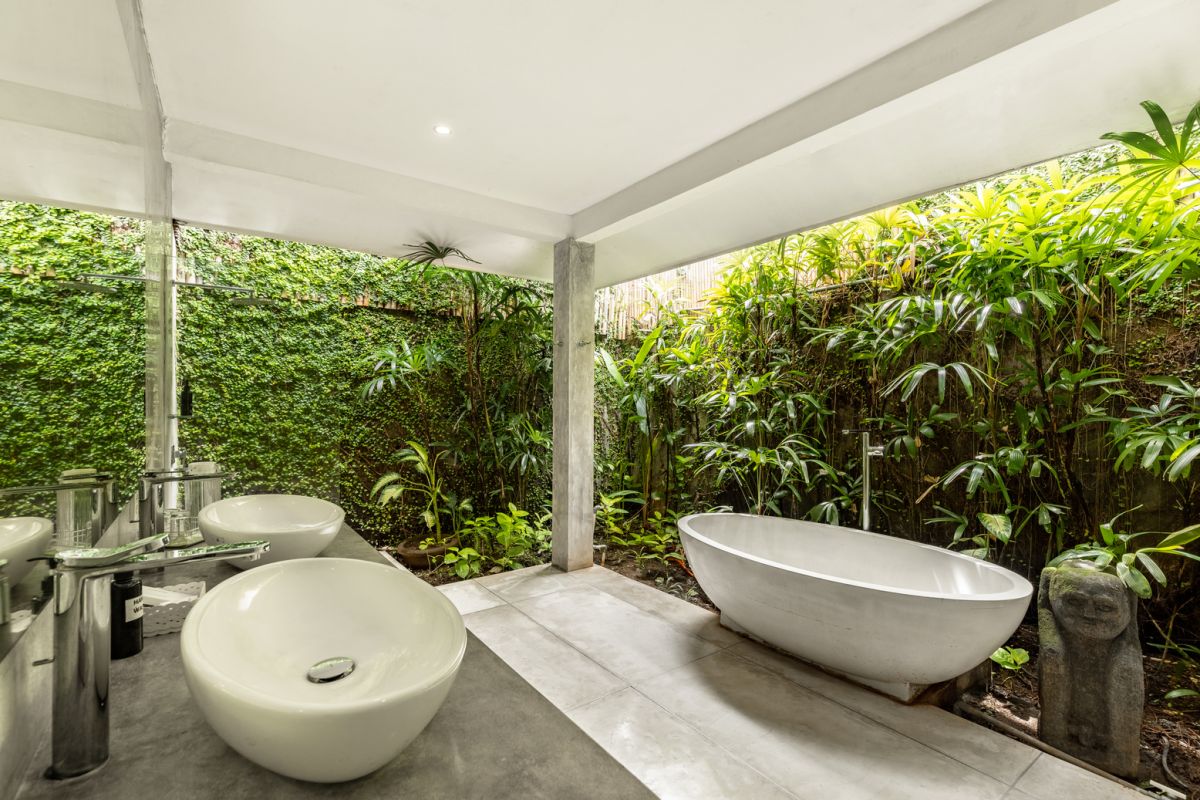 Modern white kitchen bar with concrete countertop, wooden stools, and lush tropical greenery outside arched windows. - Bali Villas