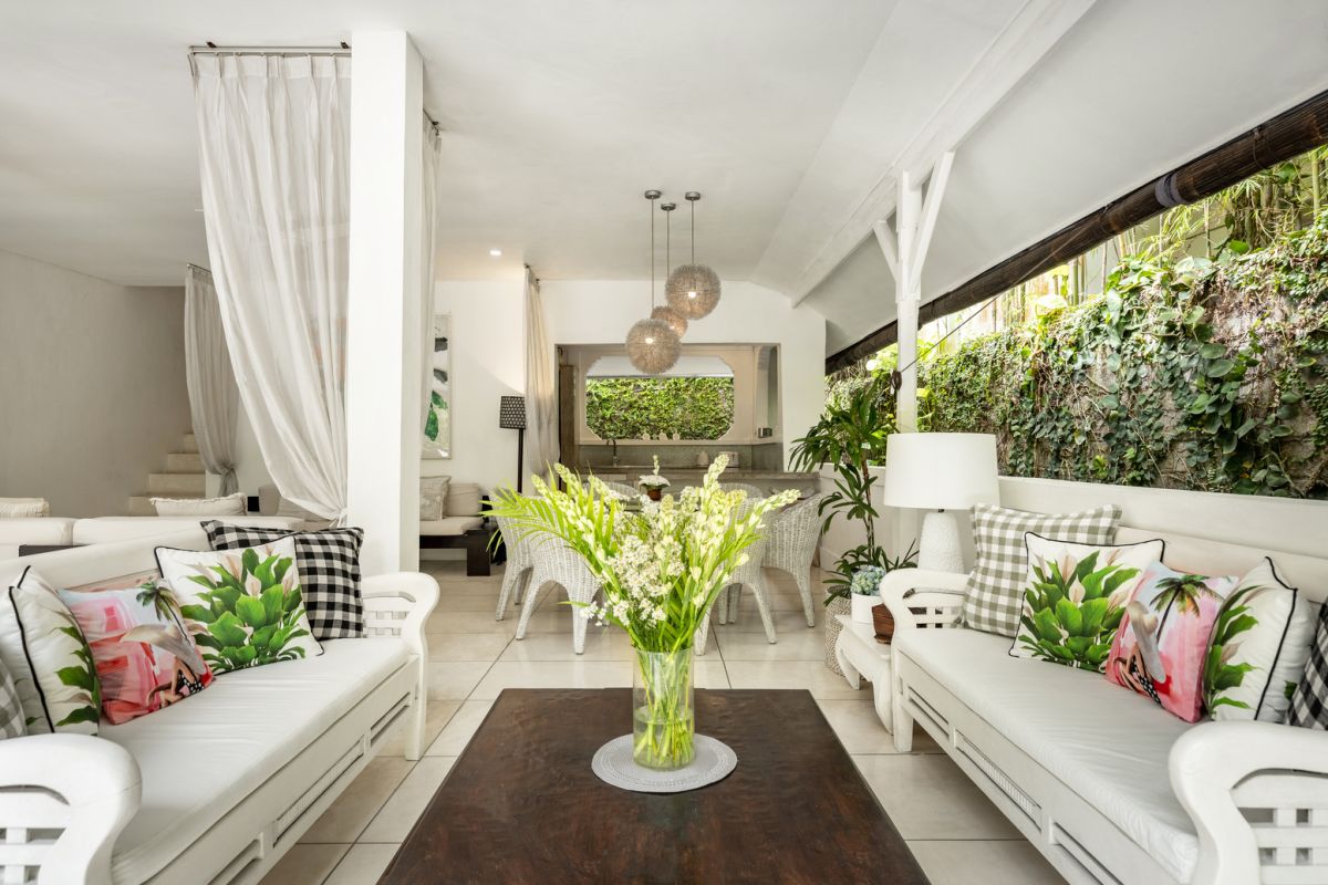 Modern white kitchen bar with concrete countertop, wooden stools, and lush tropical greenery outside arched windows. - Bali Villas