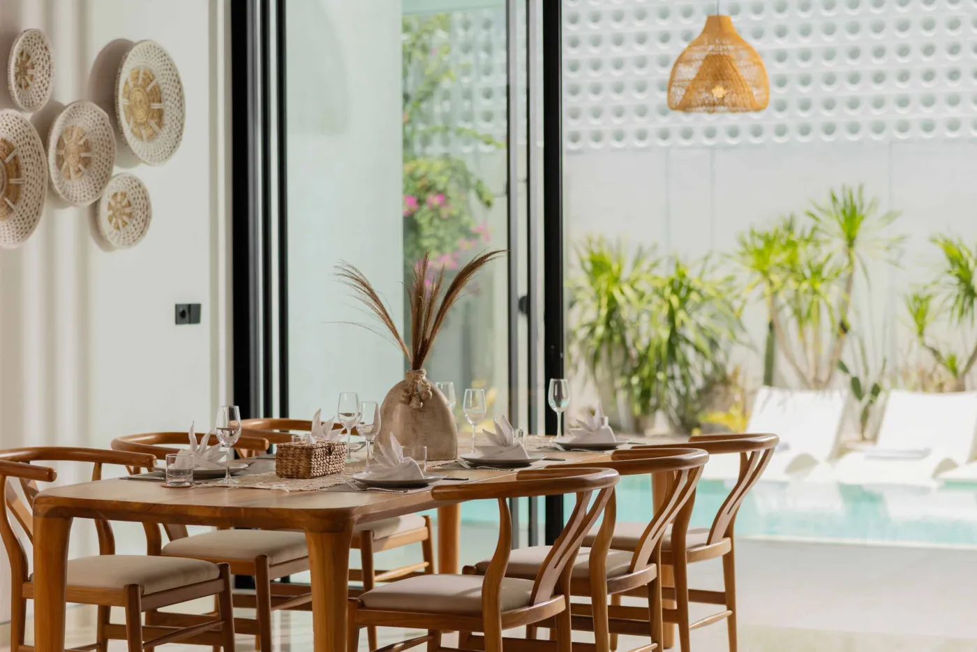 Modern game room featuring a sleek black pool table with red felt, surrounded by wooden stools, under a wooden ceiling with pendant lights, large windows showing tropical greenery, and stylish wooden accents. - Bali Villas
