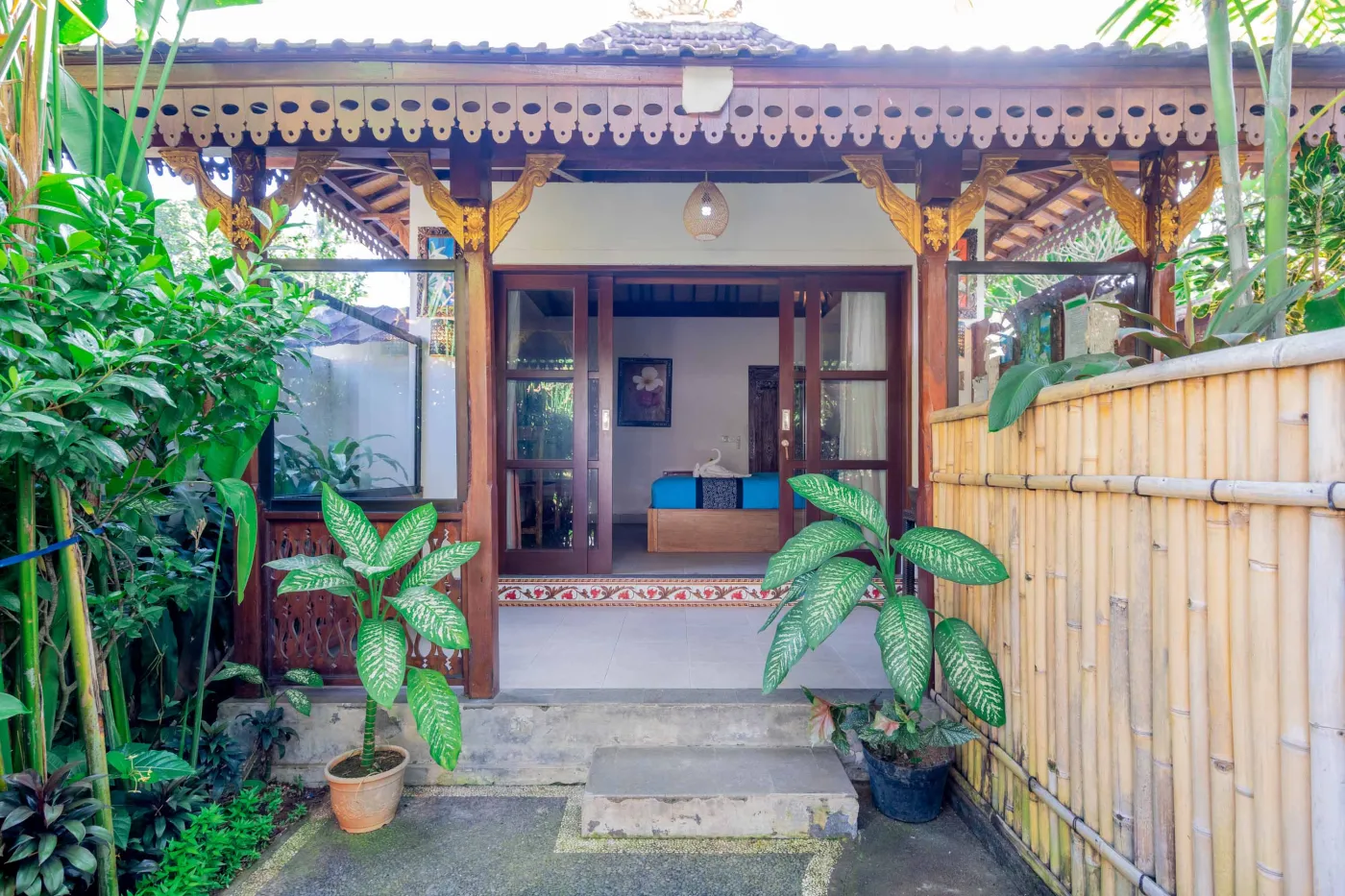 Spacious open-air Balinese pavilion with intricate carved wooden beams, hanging lanterns, rattan furniture, and tropical garden views. - Bali Villas