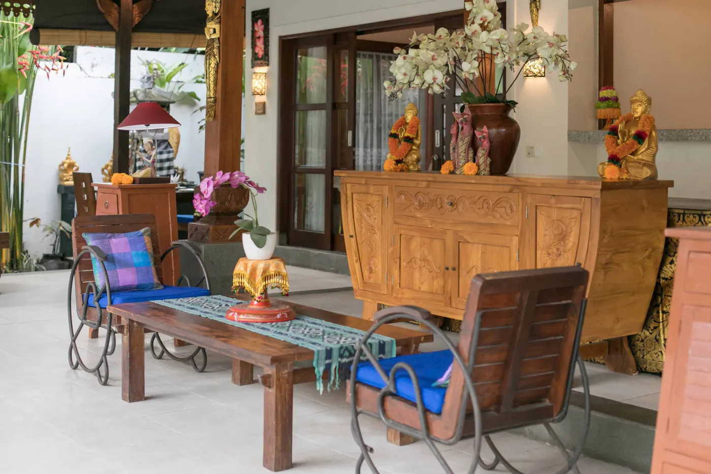Spacious open-air Balinese pavilion with intricate carved wooden beams, hanging lanterns, rattan furniture, and tropical garden views. - Bali Villas