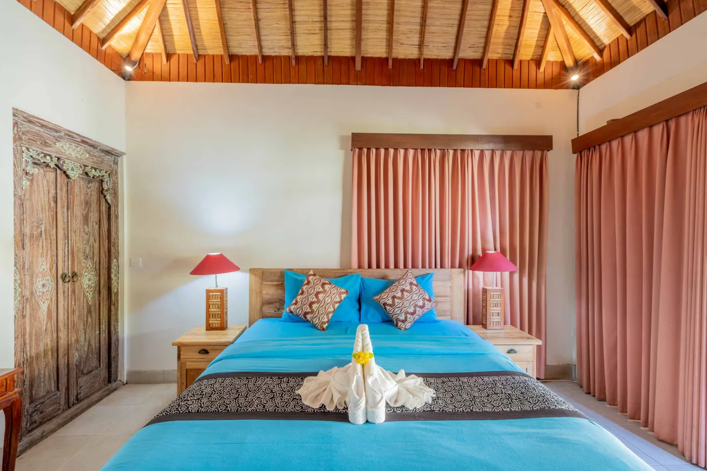 Spacious open-air Balinese pavilion with intricate carved wooden beams, hanging lanterns, rattan furniture, and tropical garden views. - Bali Villas