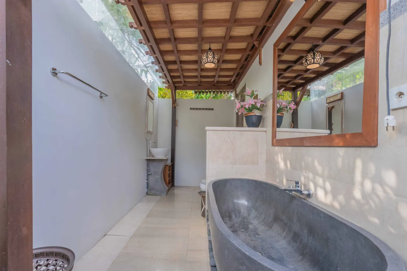 Spacious open-air Balinese pavilion with intricate carved wooden beams, hanging lanterns, rattan furniture, and tropical garden views. - Bali Villas