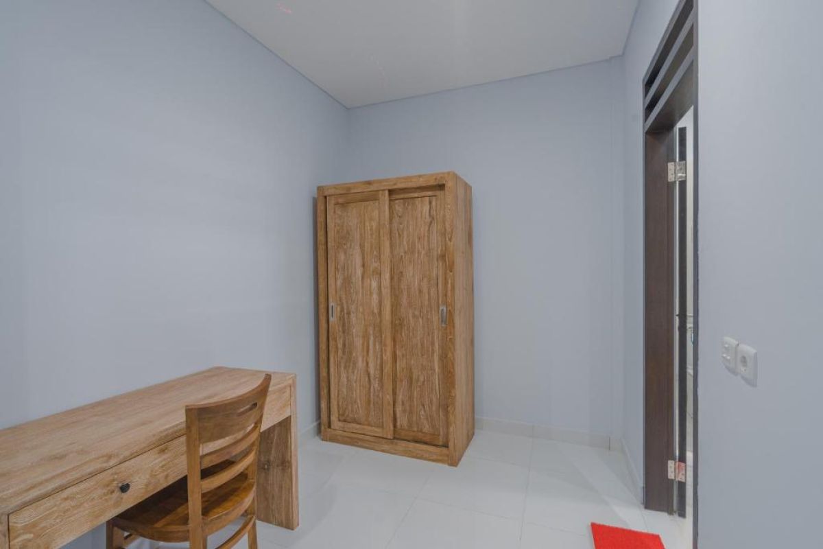 Spacious Balinese-style hotel bedroom with wooden ceiling fan, king bed, wall-mounted TV, and orange curtains. - Bali Villas