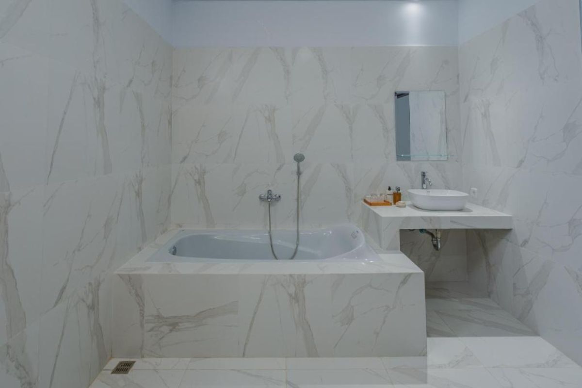 Spacious Balinese-style hotel bedroom with wooden ceiling fan, king bed, wall-mounted TV, and orange curtains. - Bali Villas