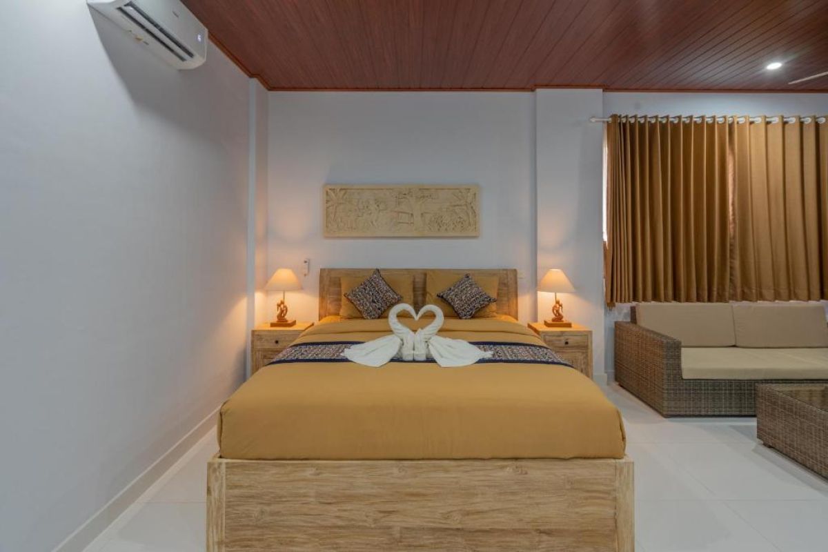Spacious Balinese-style hotel bedroom with wooden ceiling fan, king bed, wall-mounted TV, and orange curtains. - Bali Villas