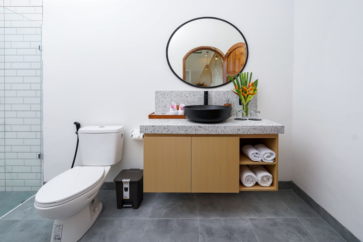 Modern tropical kitchen with curved white counter, rattan bar stools, hanging woven lamps, abstract wall art, and lush green views through large windows. - Bali Villas