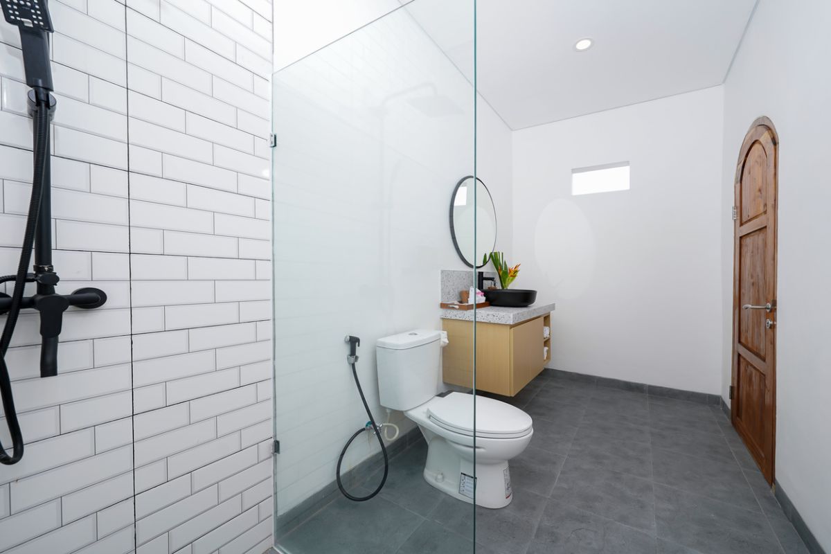 Modern tropical kitchen with curved white counter, rattan bar stools, hanging woven lamps, abstract wall art, and lush green views through large windows. - Bali Villas