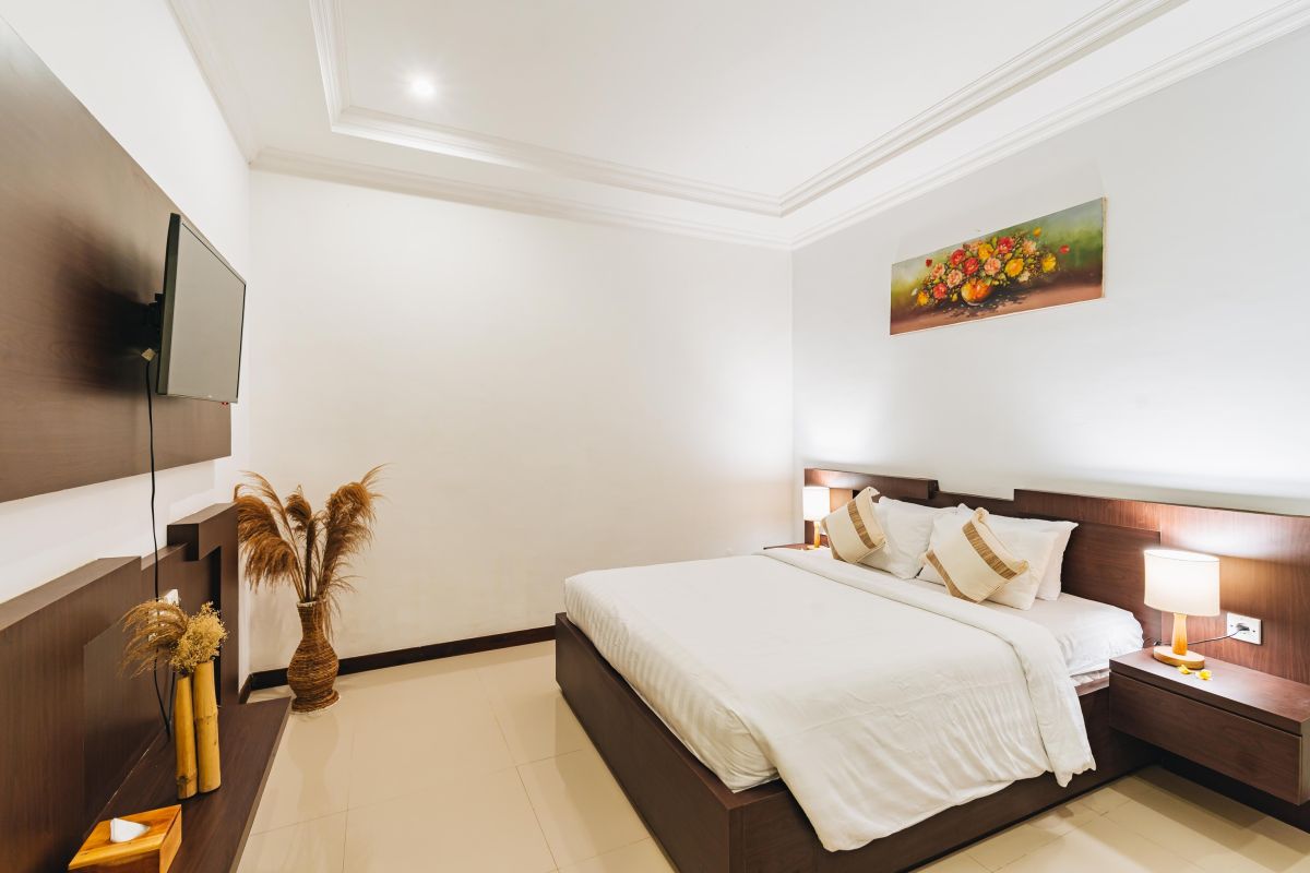 Modern Balinese living room and dining area with beige sofas, wooden table set for meal, kitchen counter, potted plants, and stairs. - Bali Villas