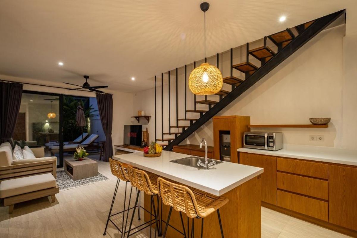 Serene tropical infinity pool at dusk with white lounge chairs, beige umbrella, and lush banana palms under soft lighting. - Bali Villas