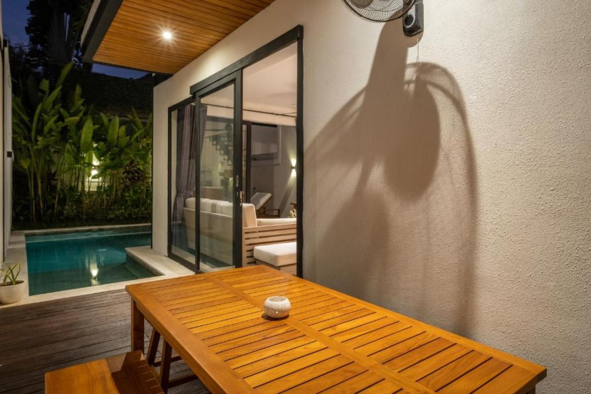 Serene tropical infinity pool at dusk with white lounge chairs, beige umbrella, and lush banana palms under soft lighting. - Bali Villas
