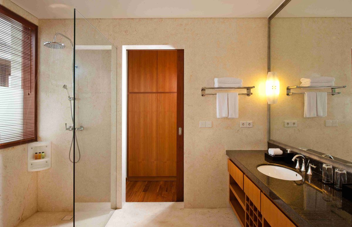 Luxurious tropical bathroom with petal-filled freestanding bathtub, lush green plants, wooden vanity, and stone shower area. - Bali Villas