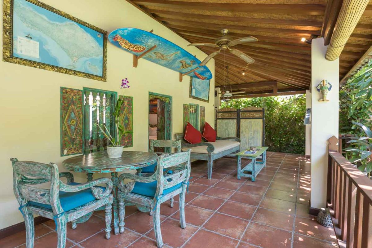 Luxurious Bali-style spa bathroom with rose-petal-filled bathtub, double black stone sinks, wooden vanities, tropical plants, and natural light from skylight. - Bali Villas