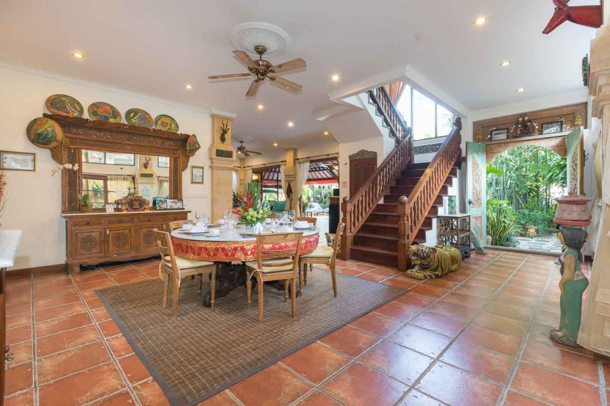 Luxurious Bali-style spa bathroom with rose-petal-filled bathtub, double black stone sinks, wooden vanities, tropical plants, and natural light from skylight. - Bali Villas