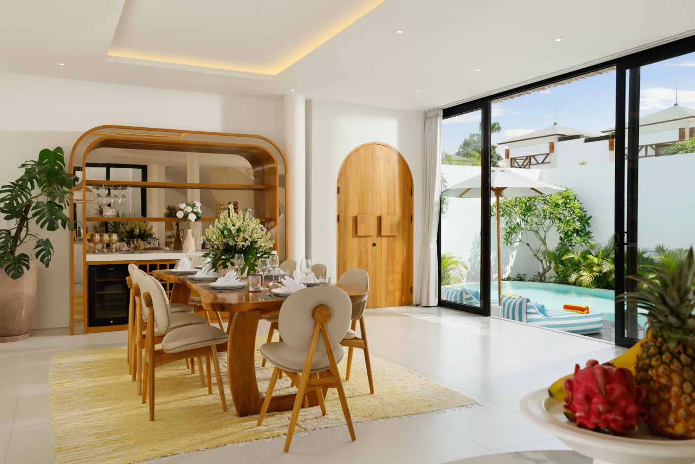 Modern minimalist bathroom with yellow flower-filled bathtub, wooden vanity, glass shower enclosure, and potted greenery. - Bali Villas