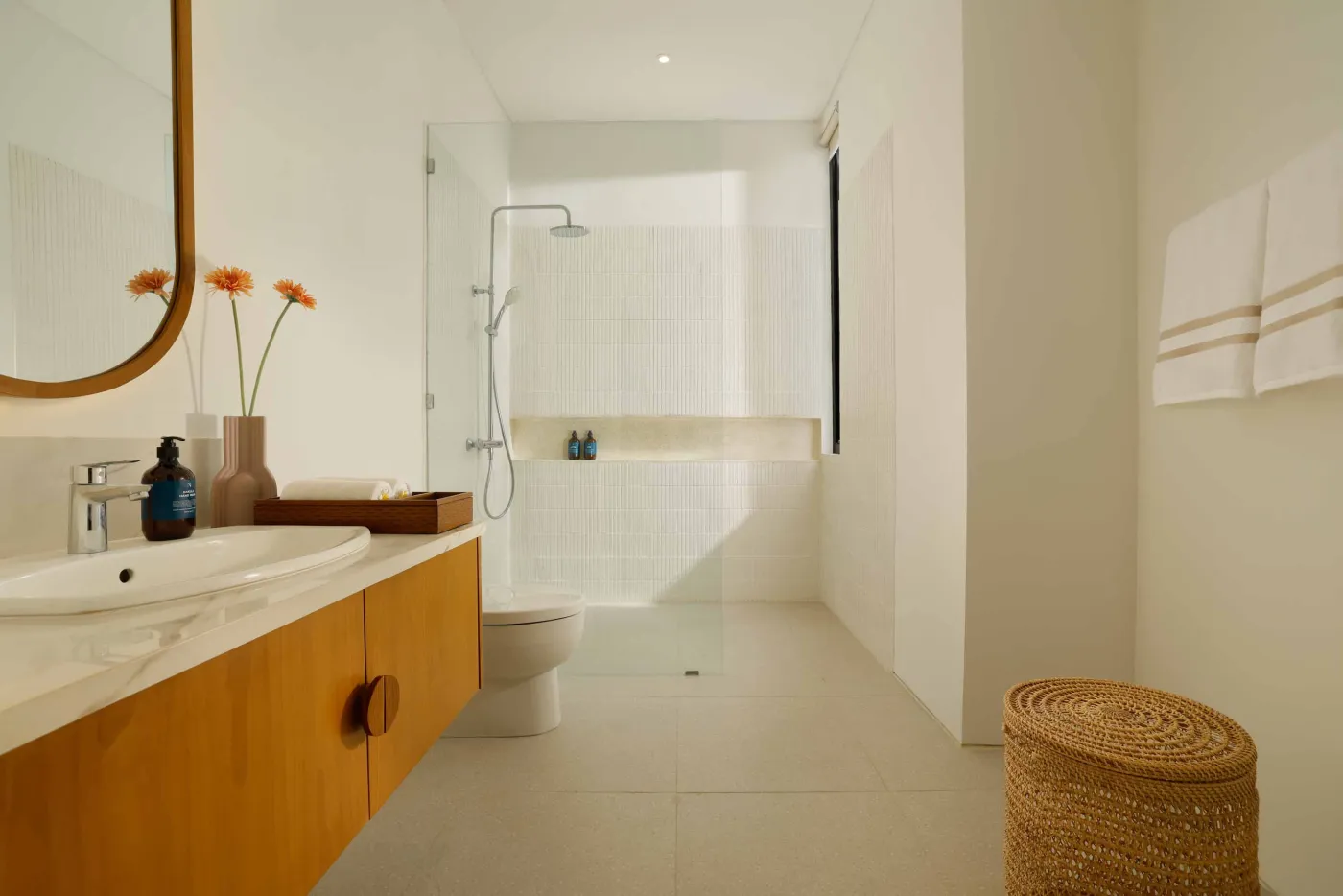 Modern minimalist bathroom with yellow flower-filled bathtub, wooden vanity, glass shower enclosure, and potted greenery. - Bali Villas