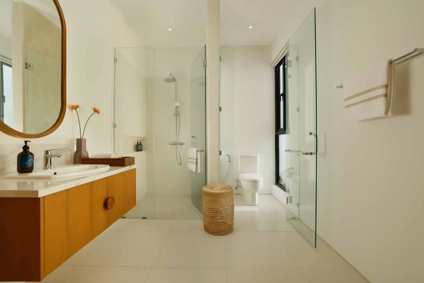 Modern minimalist bathroom with yellow flower-filled bathtub, wooden vanity, glass shower enclosure, and potted greenery. - Bali Villas