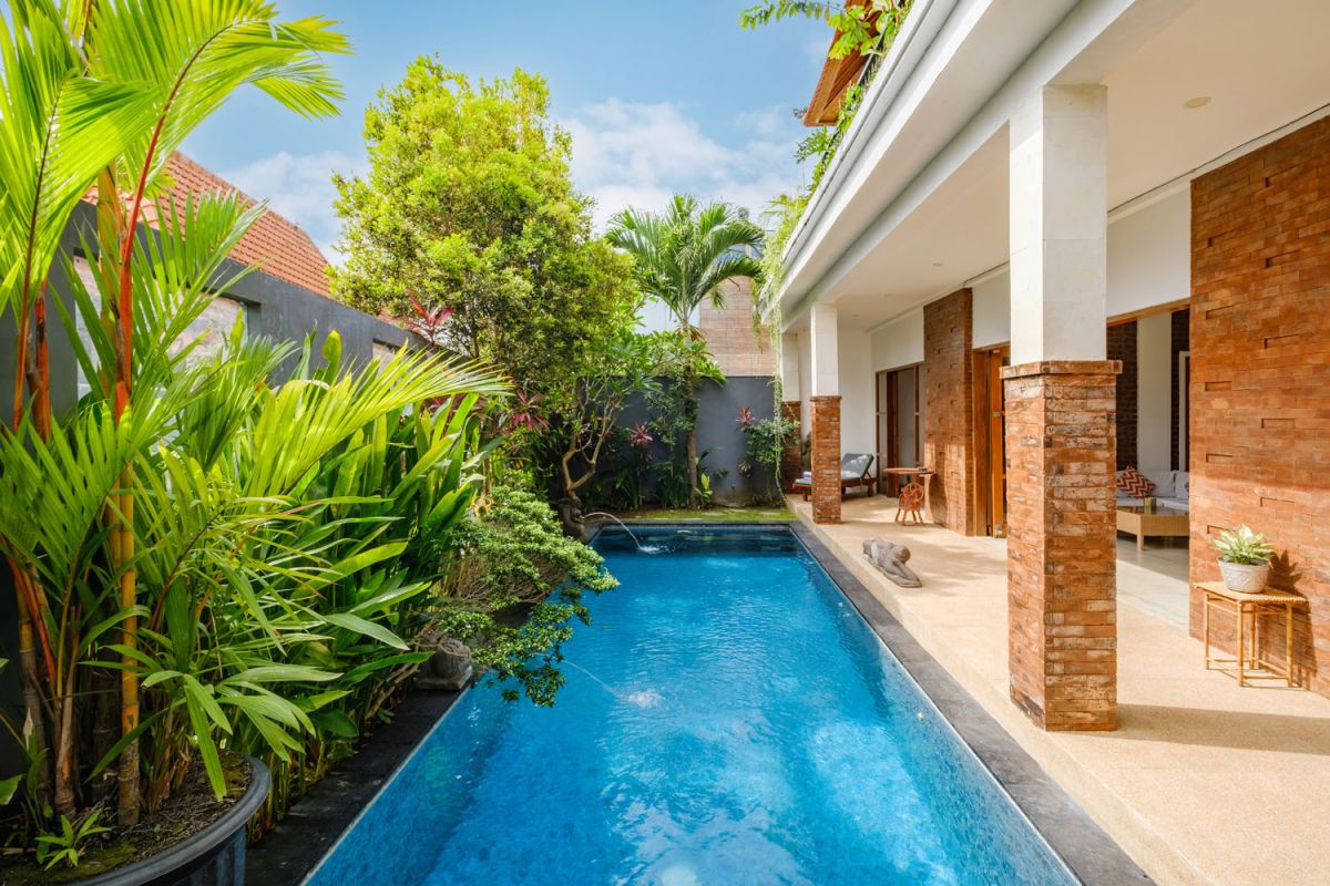 Rustic Balinese villa kitchen and dining room with wooden cabinets, stone walls, and views of traditional temple roofs. - Bali Villas