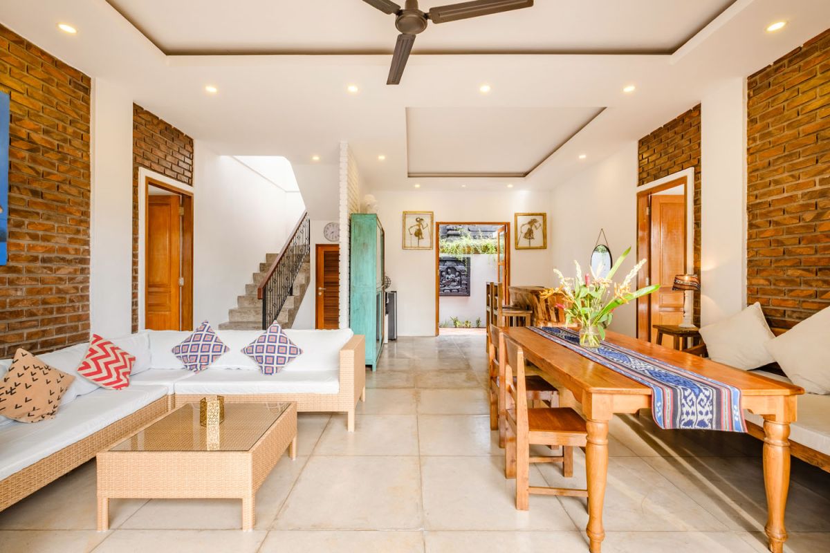 Rustic Balinese villa kitchen and dining room with wooden cabinets, stone walls, and views of traditional temple roofs. - Bali Villas