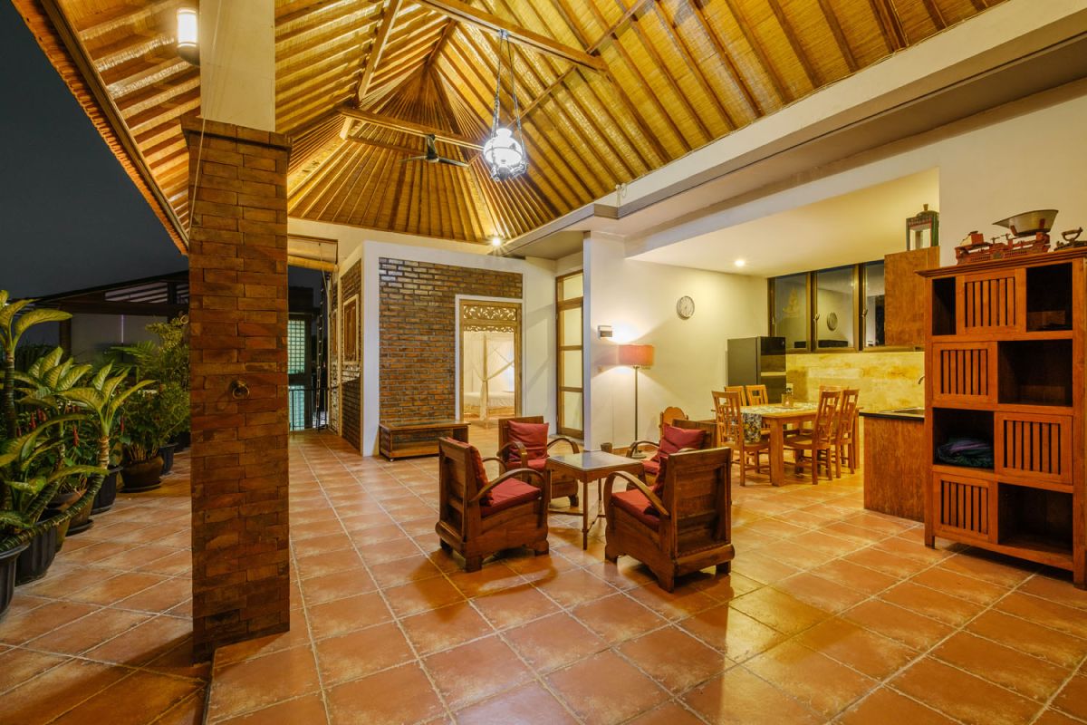 Rustic Balinese villa kitchen and dining room with wooden cabinets, stone walls, and views of traditional temple roofs. - Bali Villas