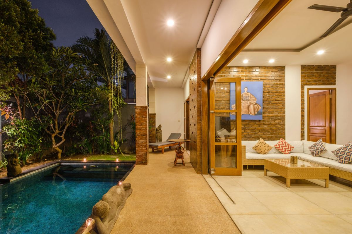 Rustic Balinese villa kitchen and dining room with wooden cabinets, stone walls, and views of traditional temple roofs. - Bali Villas