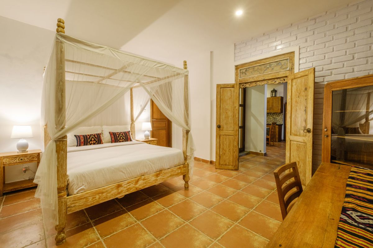 Rustic Balinese villa kitchen and dining room with wooden cabinets, stone walls, and views of traditional temple roofs. - Bali Villas